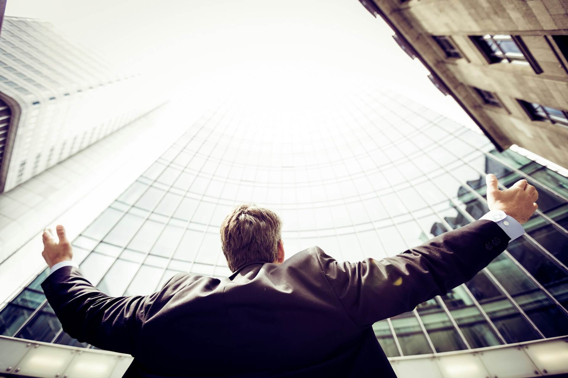 A man in a suit standing triumphantly and looking at a tall building